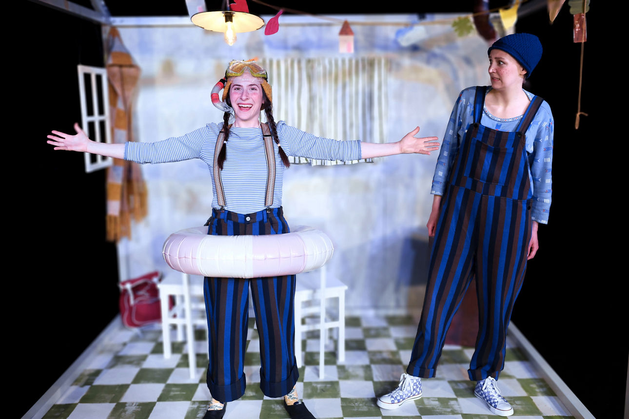Frau mit Schwimmreifen und Frau mit Latzhose steht im Esszimmer_Nimmerland Theaterproduktion