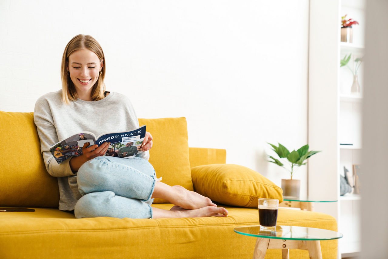 Eine junge Frau sitzt auf einem Sofa und liest eine Zeitschrift.
