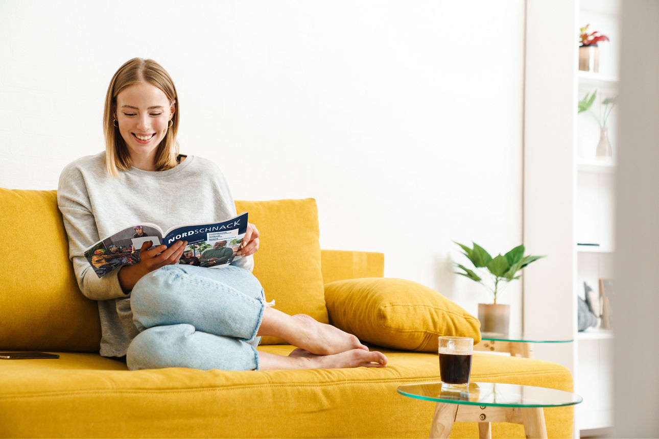 Eine junge Frau sitzt auf einem Sofa und liest eine Zeitschrift.