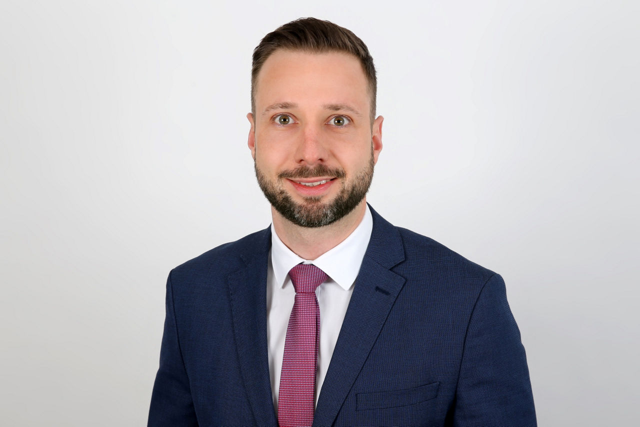 Ein lächelnder Mann in einem Anzug schaut in die Kamera.