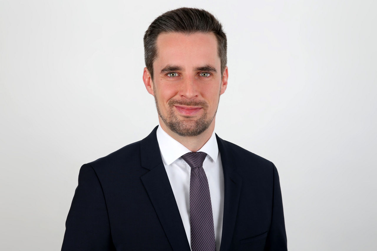 Ein lächelnder Mann in einem Anzug schaut in die Kamera.