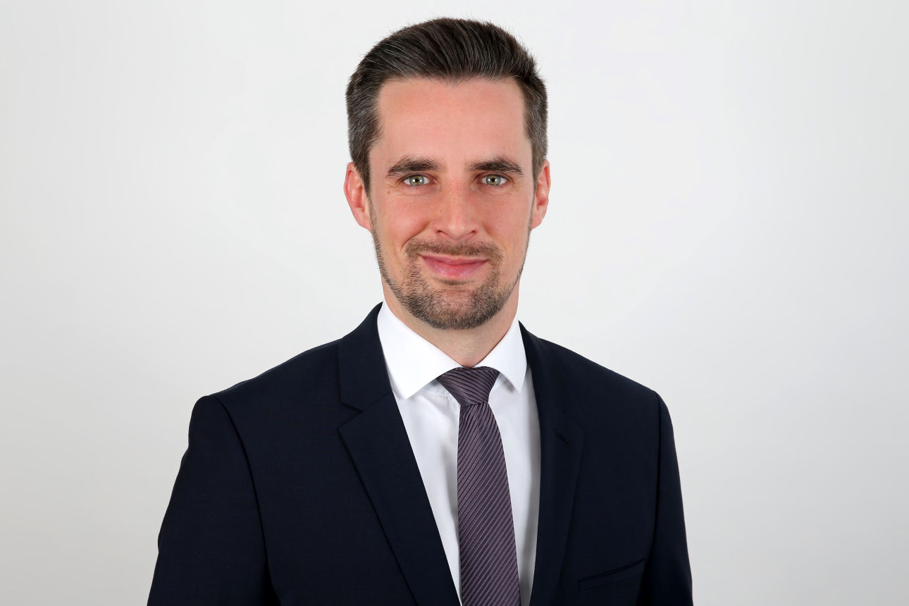 Ein lächelnder Mann in einem Anzug schaut in die Kamera.