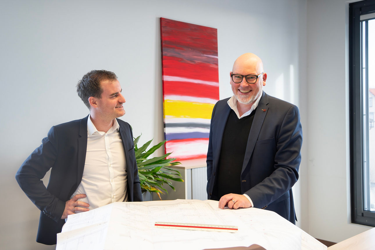Wolfgang Grath und Bernd Bischofberger stehen vor einem Tisch mit einer technischen Zeichnung. 