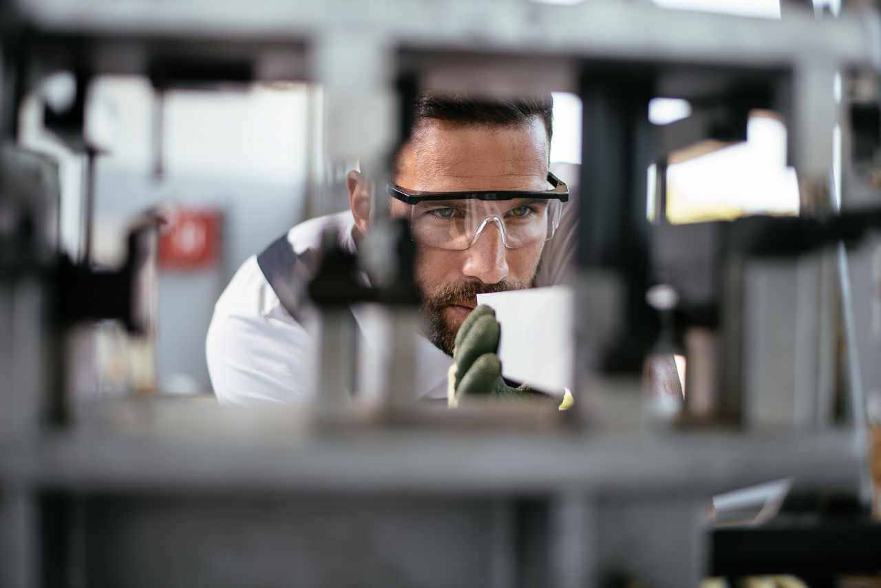 Ein Mann mit Schutzbrille arbeitet konzentriert an einer Maschine in einem Industriebetrieb.