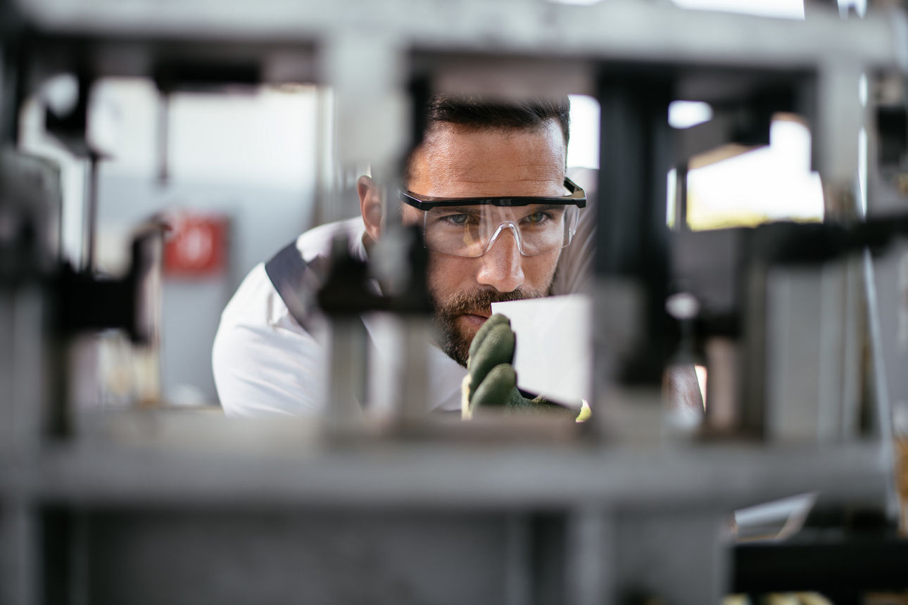 Ein Mann mit Schutzbrille arbeitet konzentriert an einer Maschine in einem Industriebetrieb.