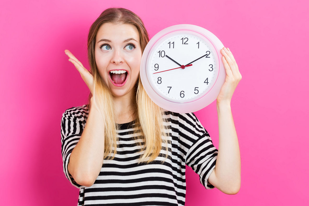 Junge Frau mit Uhr in der Hand vor pinkem Hintergrund.