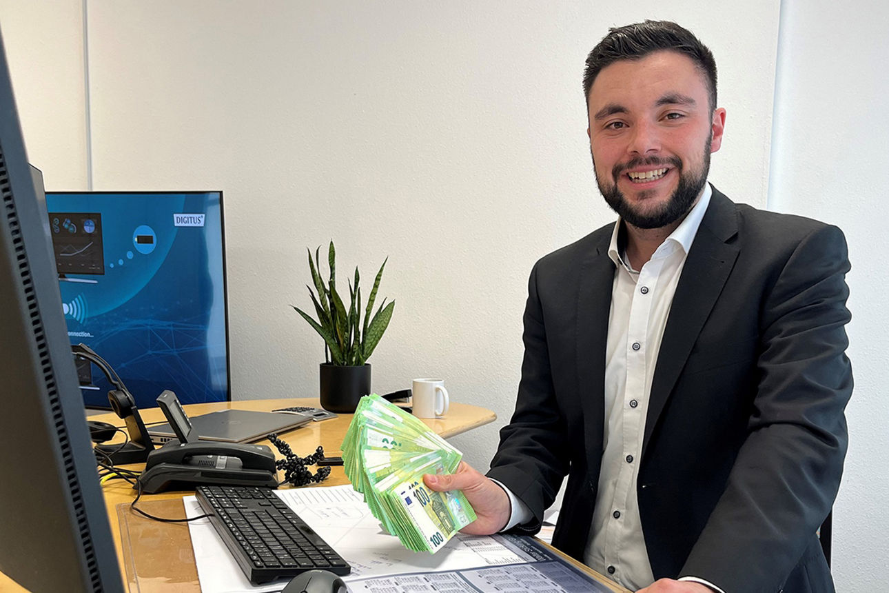 Kundenberater sitzt lächelnd am Schreibtisch und hält den Geldgewinn in seinen Händen.