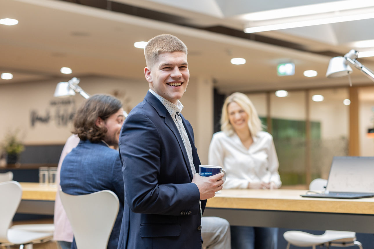 Ein junger Mann steht mit einer Tasse in der Hand vor einem Tresentisch