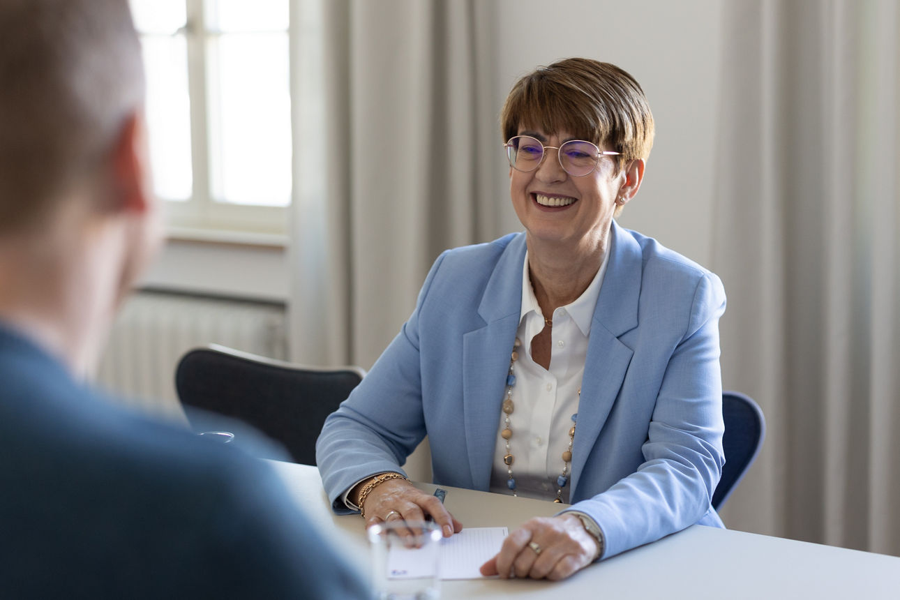 Eine lächelnde Frau sitzt an ihrem Arbeitsplatz