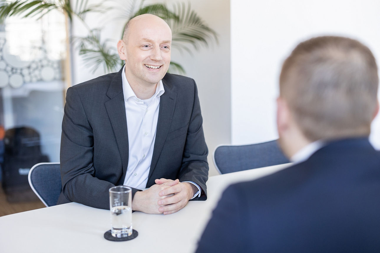 Ein Bankmitarbeiter sitzt an einem Tisch und lächelt