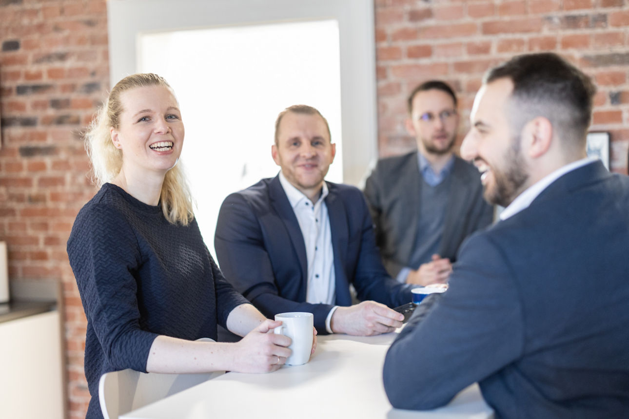 Eine Gruppe von Bankmitarbeitenden steht an einem Tisch und lacht