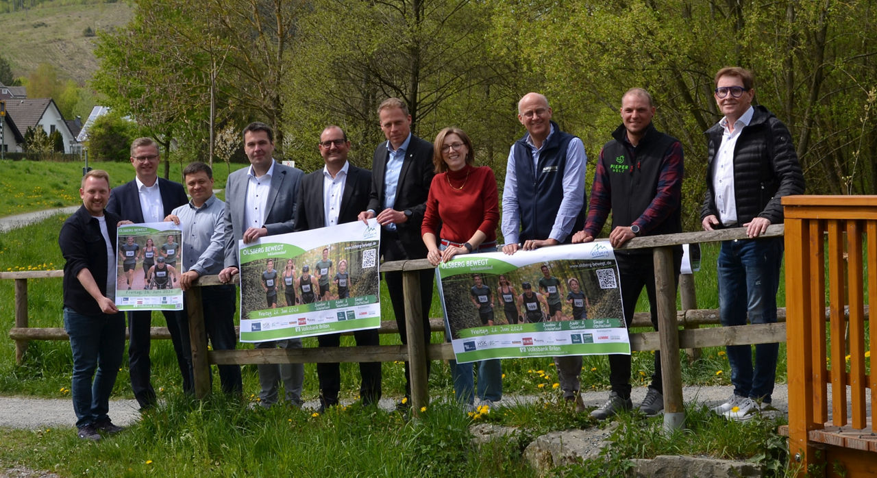 Organisatoren und Unterstützer des Inklusionslaufes in Olsberg stehen in der Natur und halten Veranstaltungsplakate in den Händen.