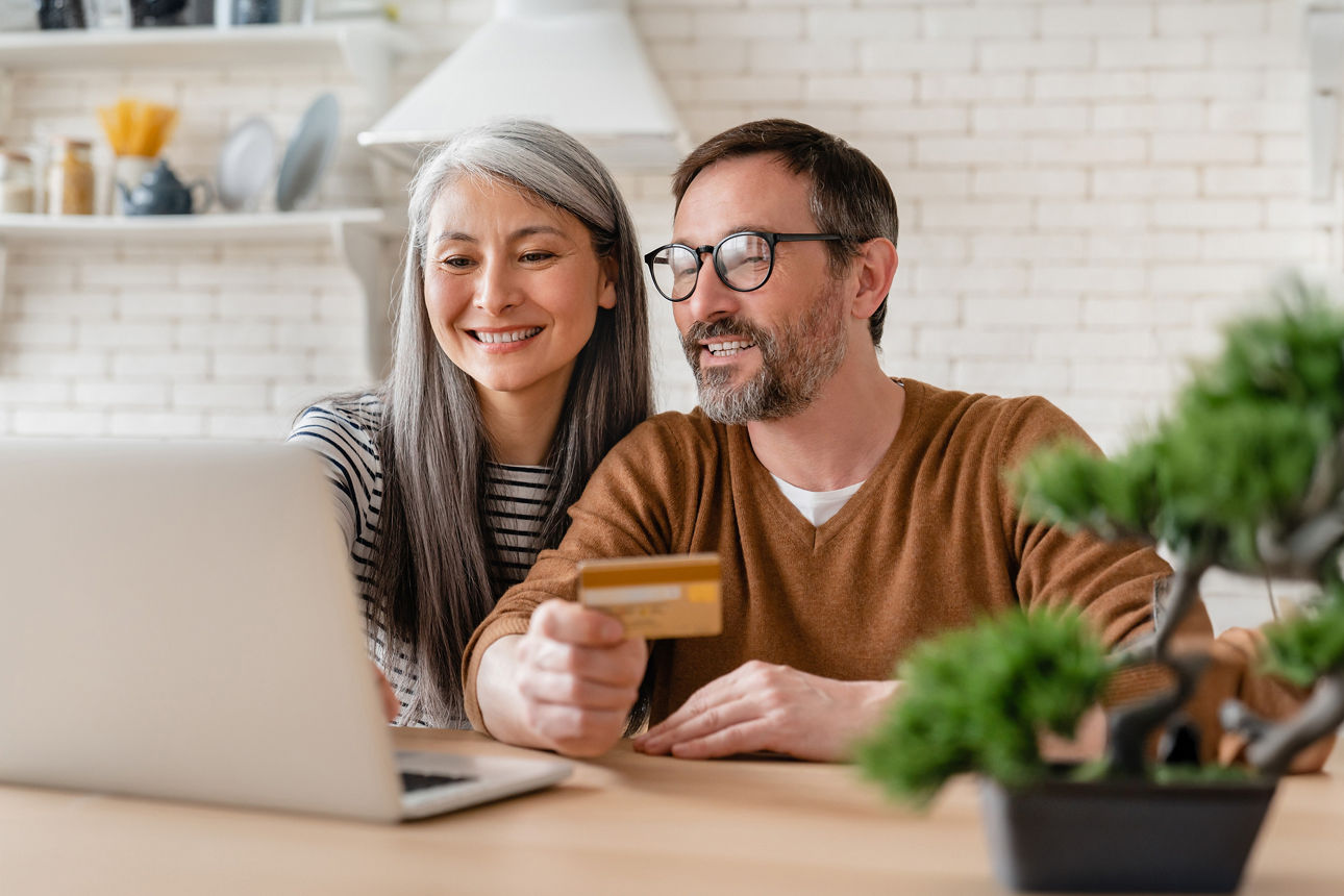 Ehepaar mit Laptop und Bankkarte sitzt am Küchentisch