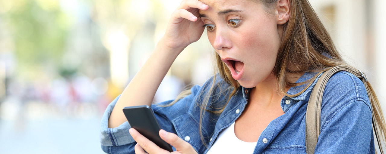 Frau fasst sich entsetzt vor den Kopf mit Blick aufs Handy