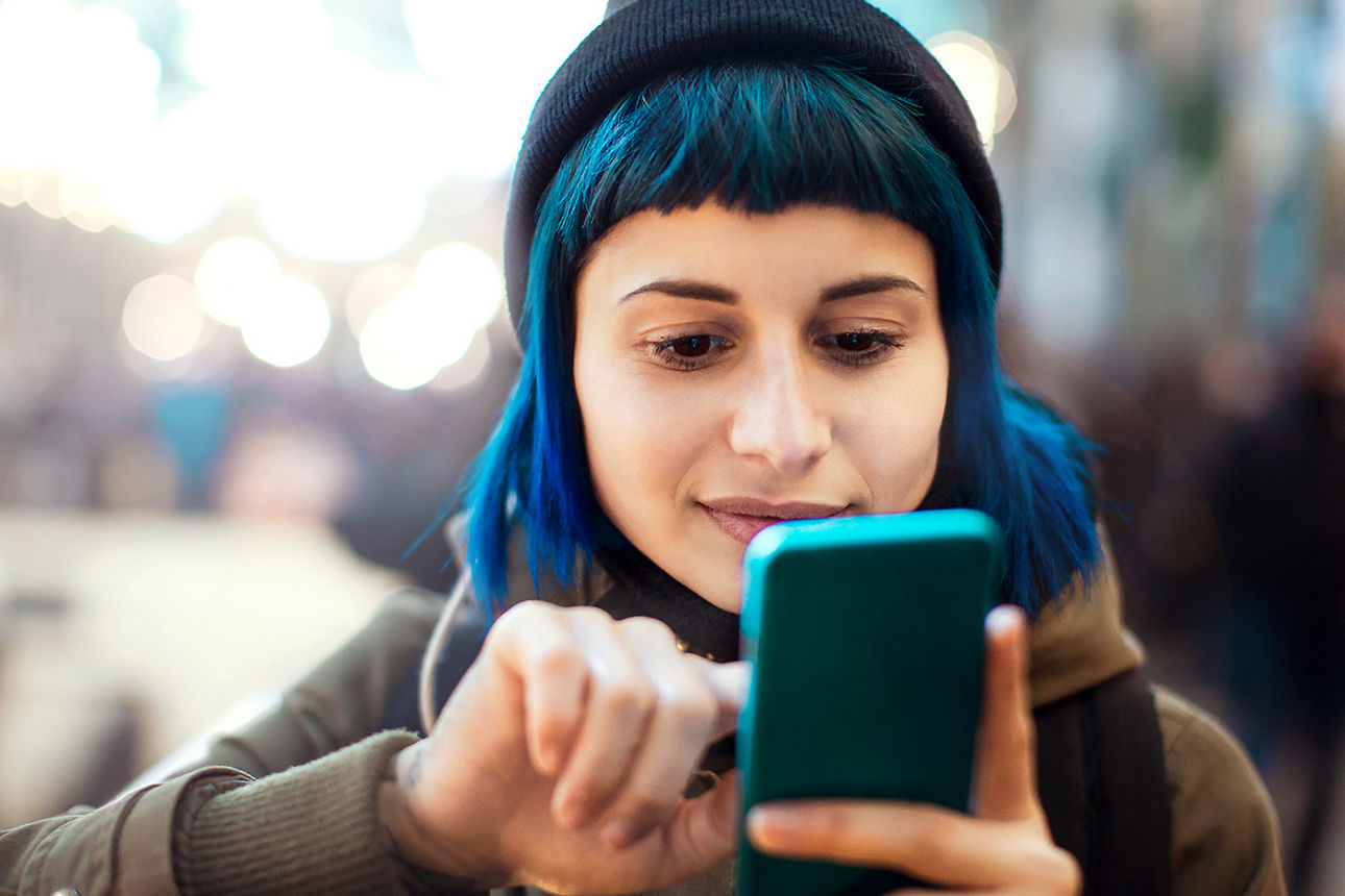 Junge Frau mit blauen Haaren scrollt auf ihrem Handy