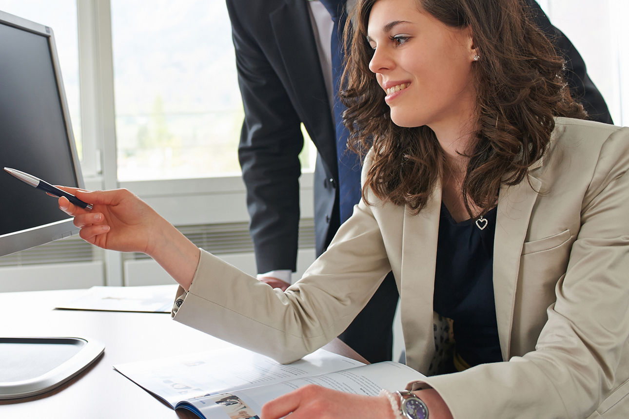 Bankmitarbeiterin deutet mit einem Stift auf einen Monitor