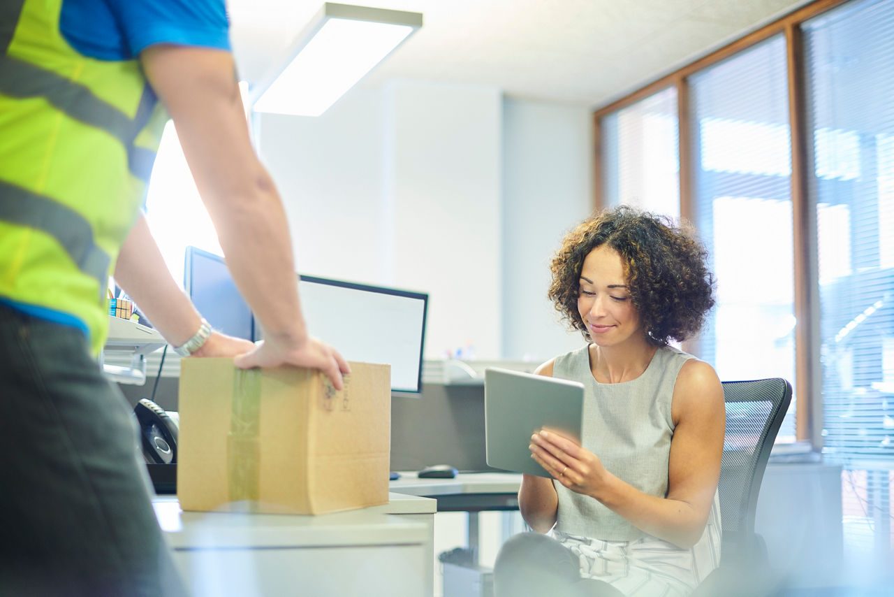 Eine Frau mit lockigem Haar sitzt in einem Büro und schaut auf ein Tablet