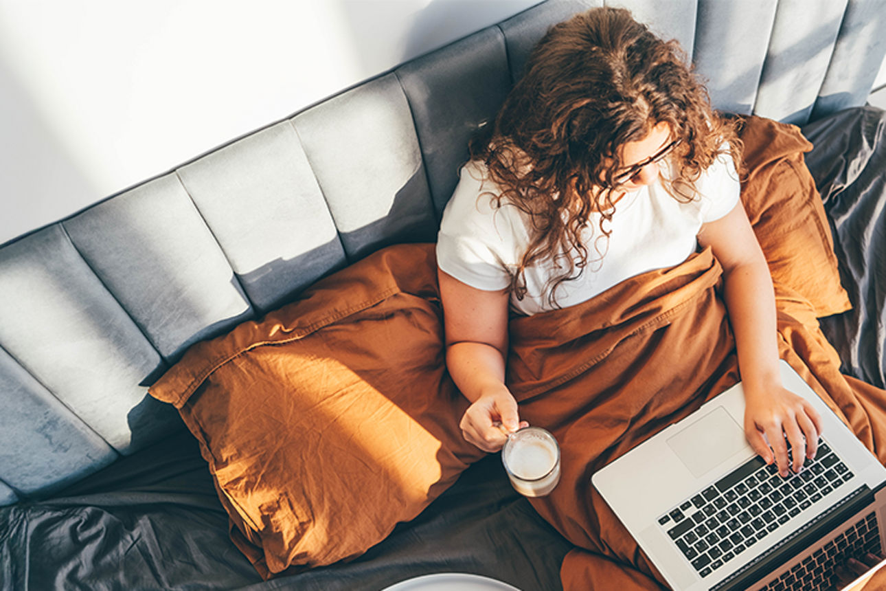 Frau sitzt mit Laptop und Kaffee im Bett – Symbolbild für bequemes Online-Tagesgeld und digitale Finanzverwaltung.