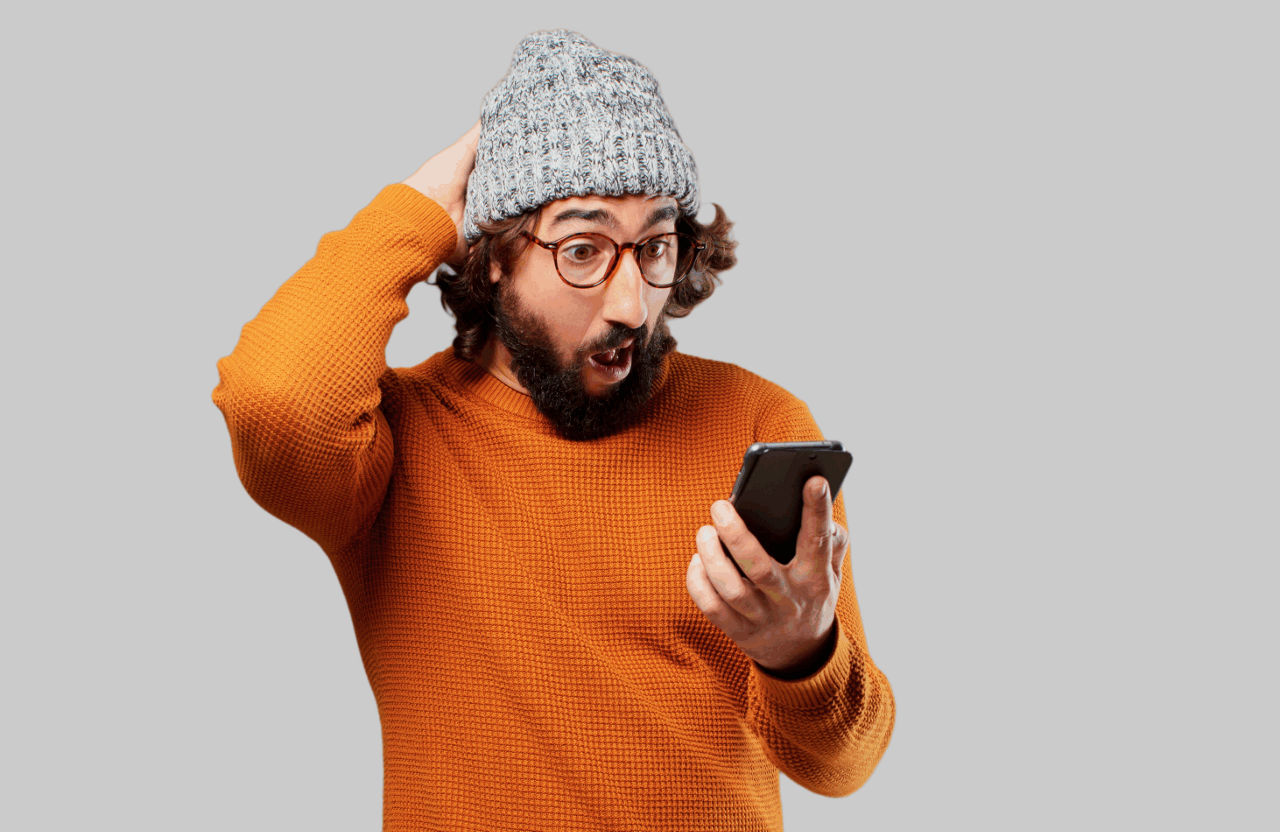 Mann im orangen Pullover schaut erstaunt auf sein Handy