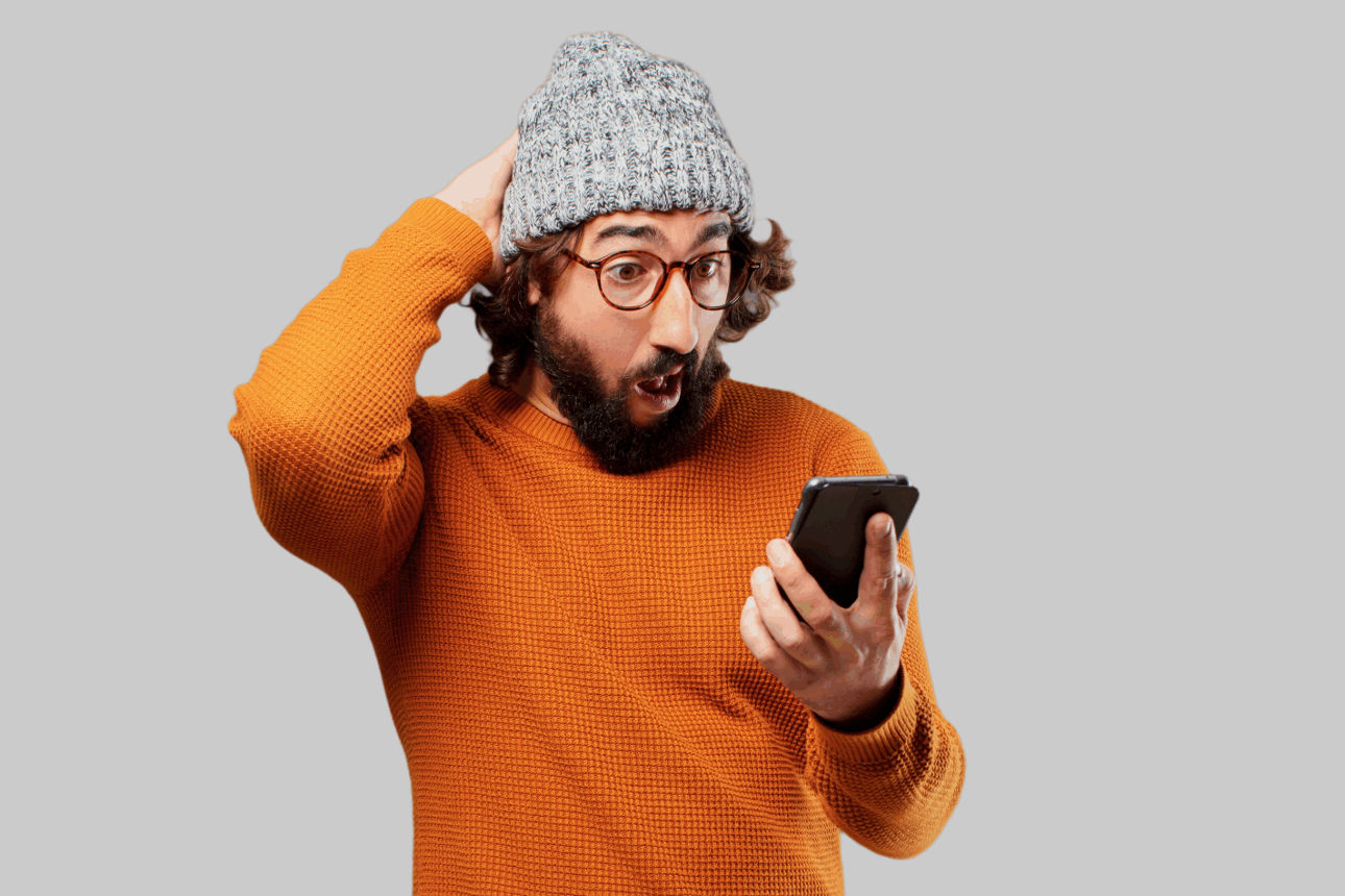 Mann im orangen Pullover schaut erstaunt auf sein Handy