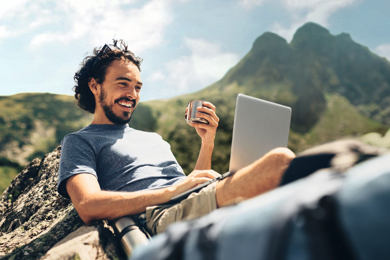 Mann in den Bergen mit Laptop auf dem Schoß