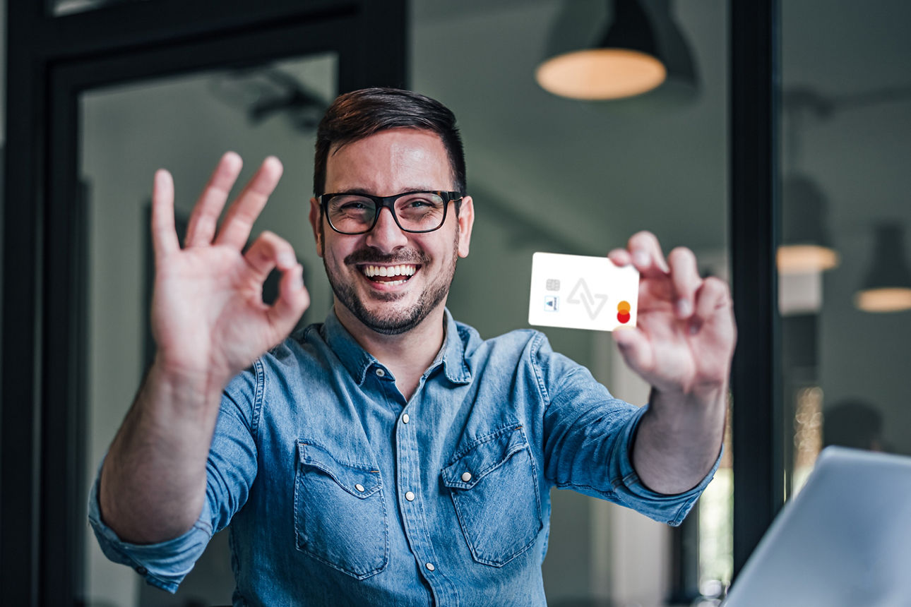 Abbildung zeigt einen fröhlichen Mann mit Brille, welcher die girocard von Meine Bank in der Hand hält.
