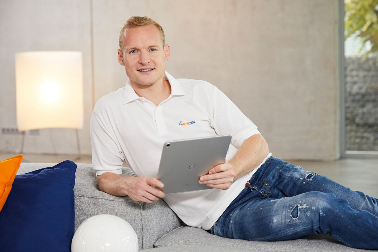 Abbildung zeigt Sebastian Rode (ehemaliger Fußballspieler), welcher auf der Couch sitzt und sein Tablet in der Hand hält