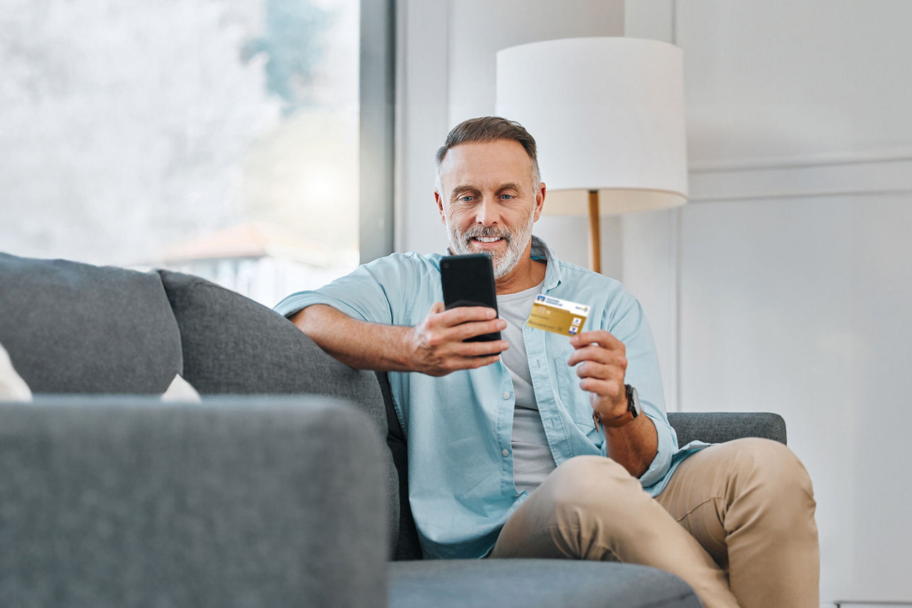 Credit card, mobile phone and mature man on sofa for transaction, e commerce or online shopping in living room. Payment, smartphone and person for purchase, subscription or internet banking in home.