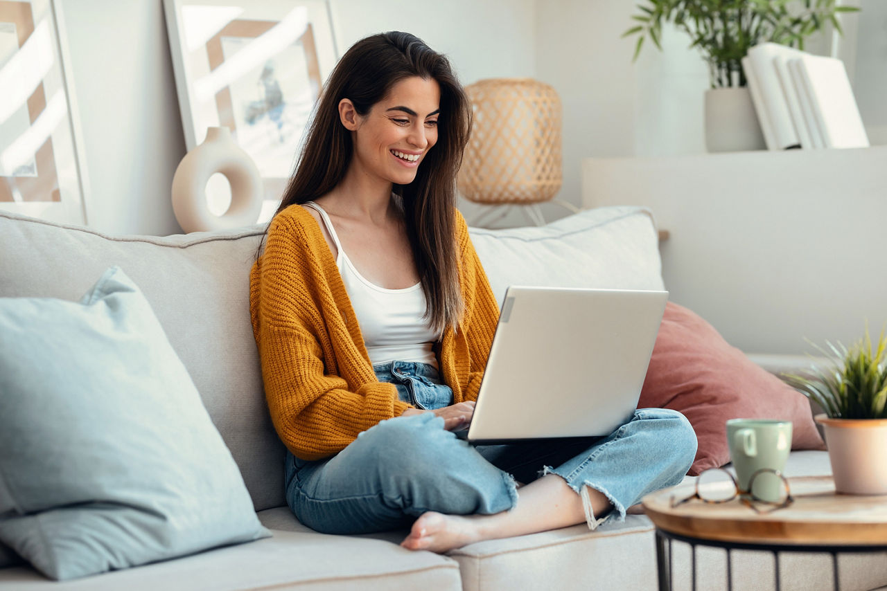 Schöne junge Frau, die zu Hause auf einem Sofa sitzt und auf ihren Laptop guckt.