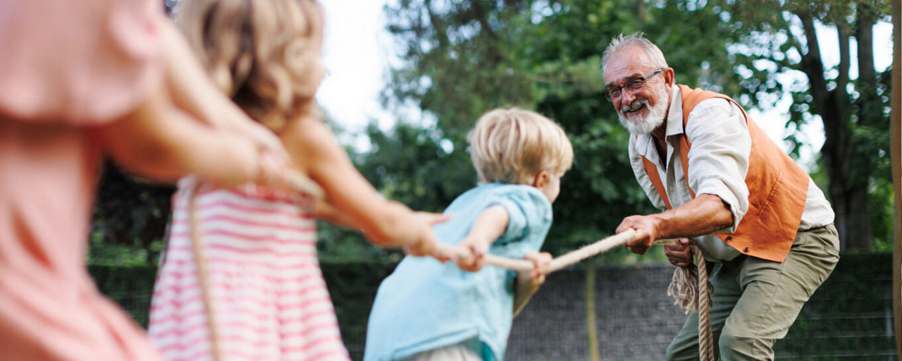 Opa spielt mit seinen Enkeln im Garten Tauziehen.