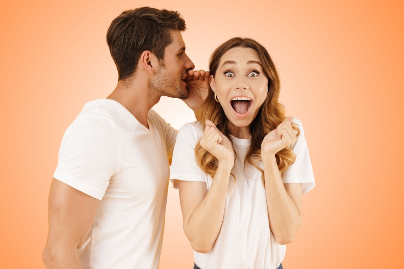 Ein junger Mann flüstert etwas Freudiges in das Ohr einer jungen Dame