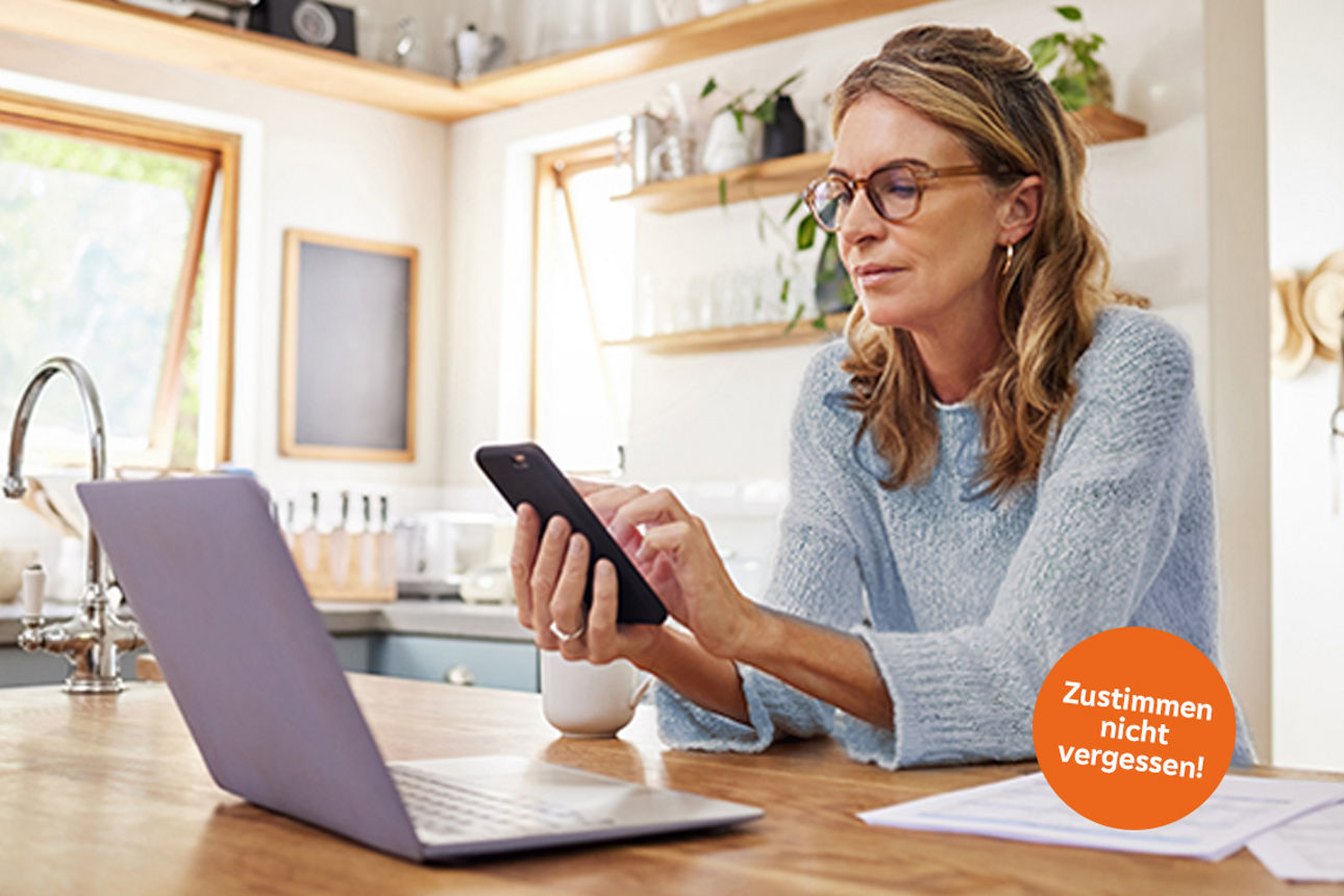 Frau schaut aufs HAndy in ihrer küche und überlegt