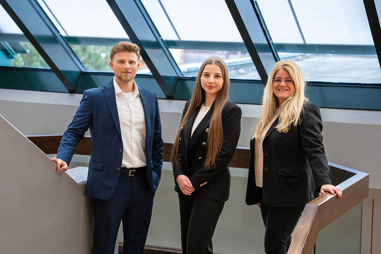 Ein Mann und zwei Frauen stehen vor einer Glasfront