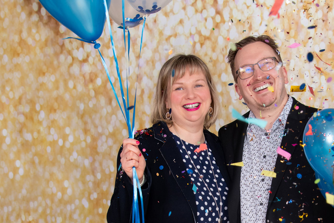 Blonde Frau steht links neben Mann mit Brille