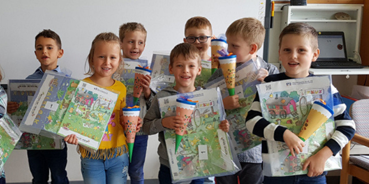 Eine Gruppe Erstklässler halten Malblöcke und Mini-Schültüten in der Hand.