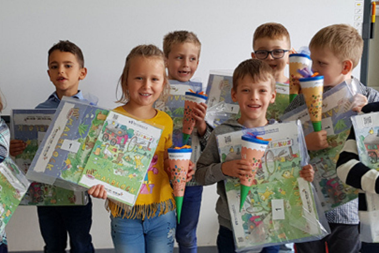 Eine Gruppe Erstklässler halten Malblöcke und Mini-Schültüten in der Hand.