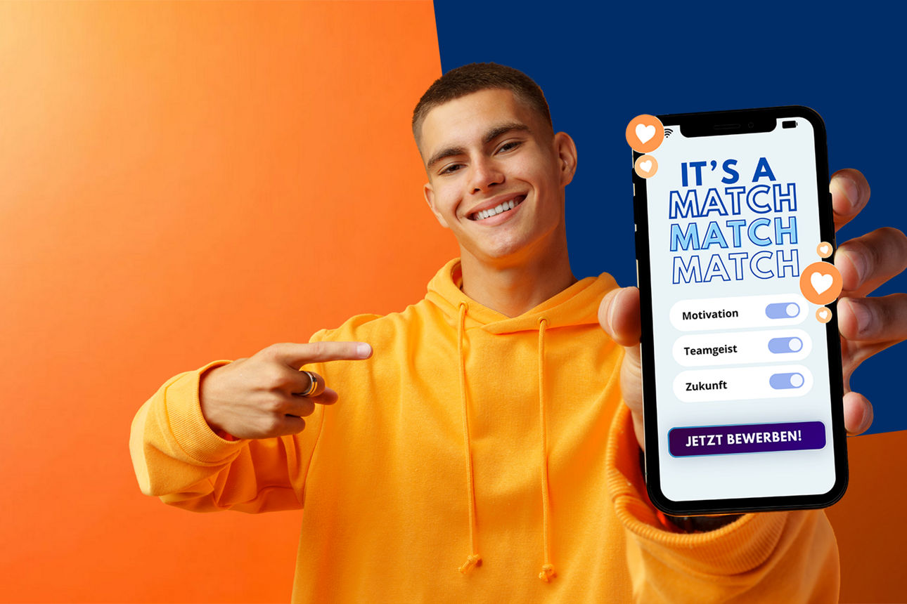 Junger Mann mit orangefarbenem Pulli zeigt auf ein Handy mit der Aufschift: It's a Match
