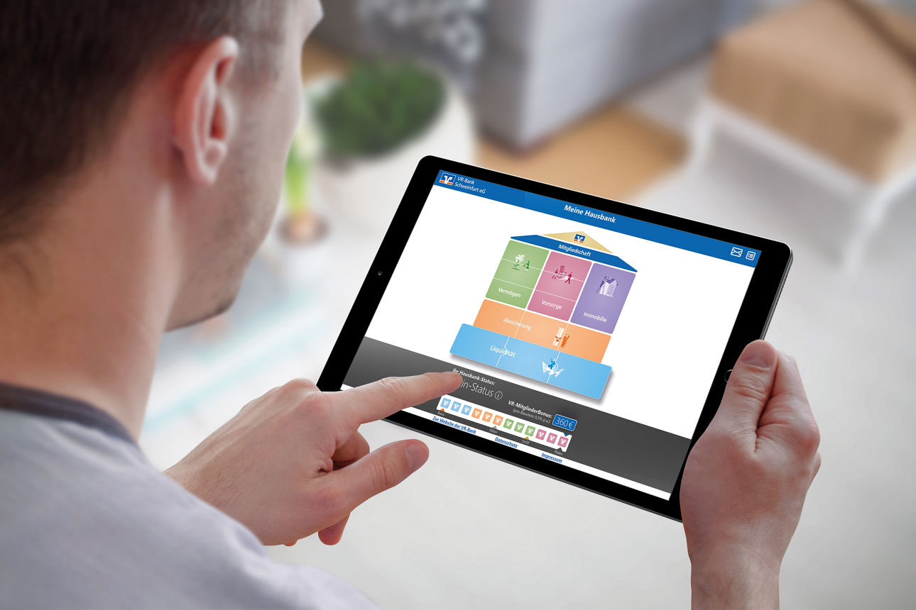 Mann schaut auf sein Tablet. Zu sehen ist das Haus für unser Bausteinprinzip