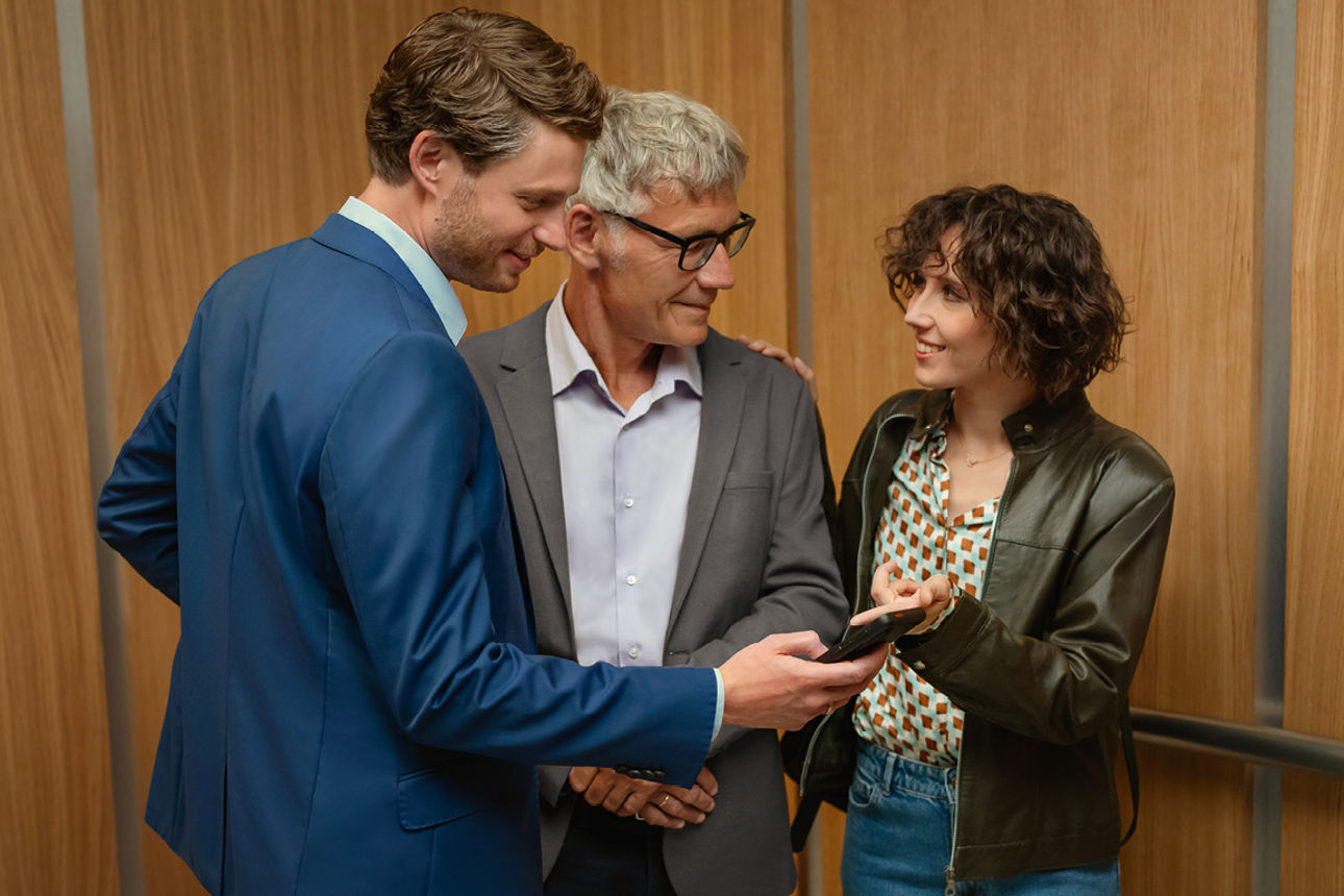 Drei Personen unterhalten sich angeregt und schauen in ein Handy um etwas zu besprechen.