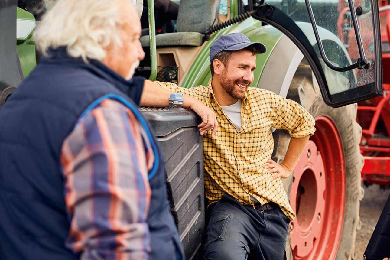 Drei Personen im Gespräch vor einem Traktor, darunter ein Landwirt und zwei Berater.
