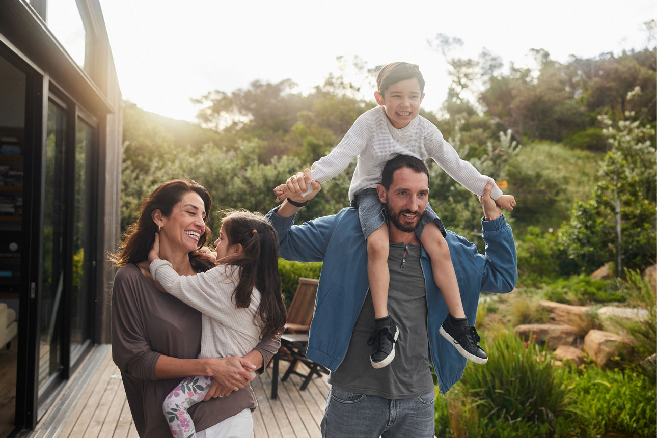 Familie freut sich vor dem Wohnhaus im Sonnenschein