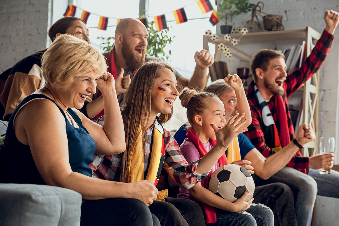 Familie sitzt auf Sofa mit deutschen Fanartikeln und jubelt.
