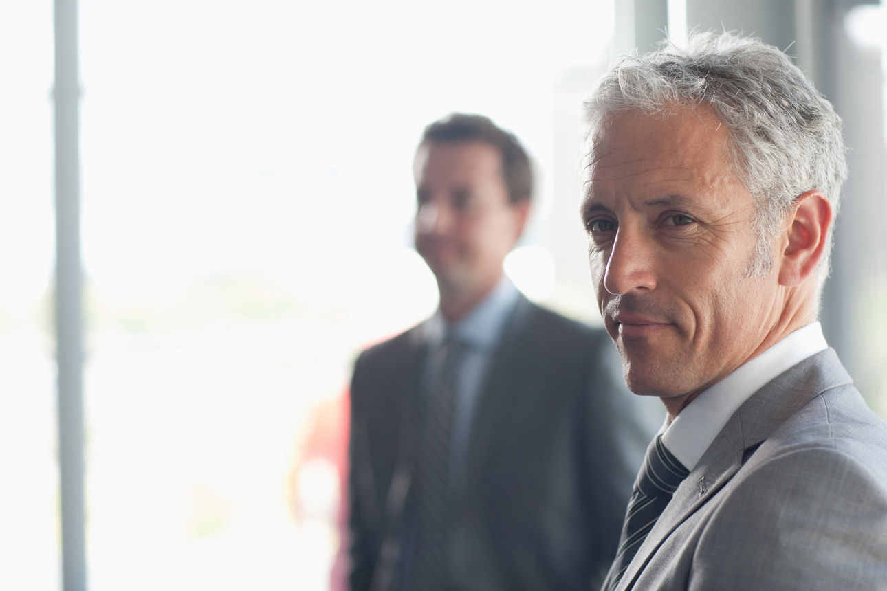 Zwei Herren im Anzug vor einem weißen Hintergrund.