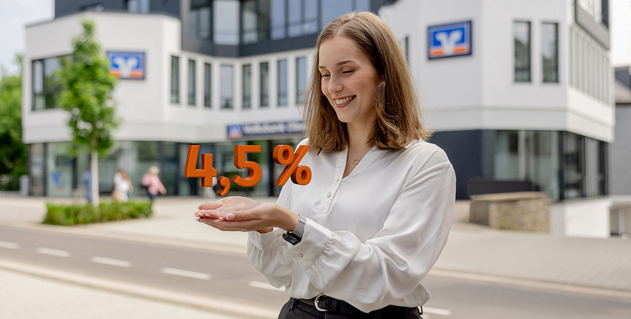 Junge Frau steht lächelnd vor einem modernen Bankgebäude und hält die Zahl „4,50%“ in orangefarbener Schrift scheinbar in ihren Händen.