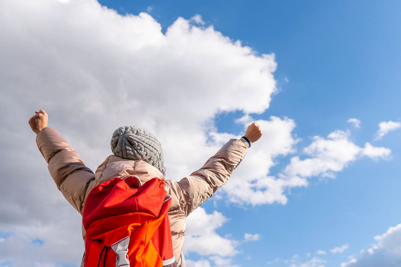 Frau steht auf einem Berg und streckt Arme hoch