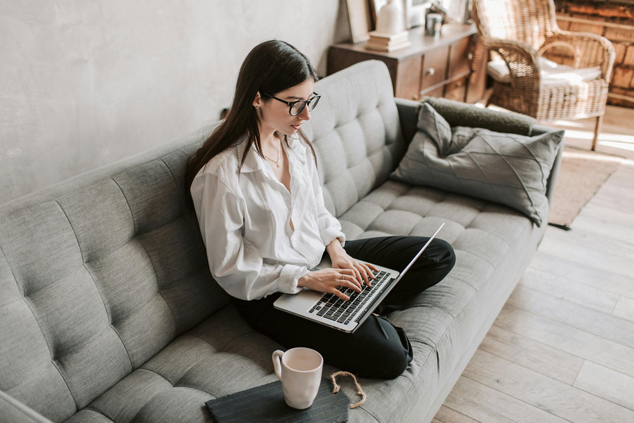 Eine junge Frau sitzt auf einem Sofa und arbeitet am Laptop