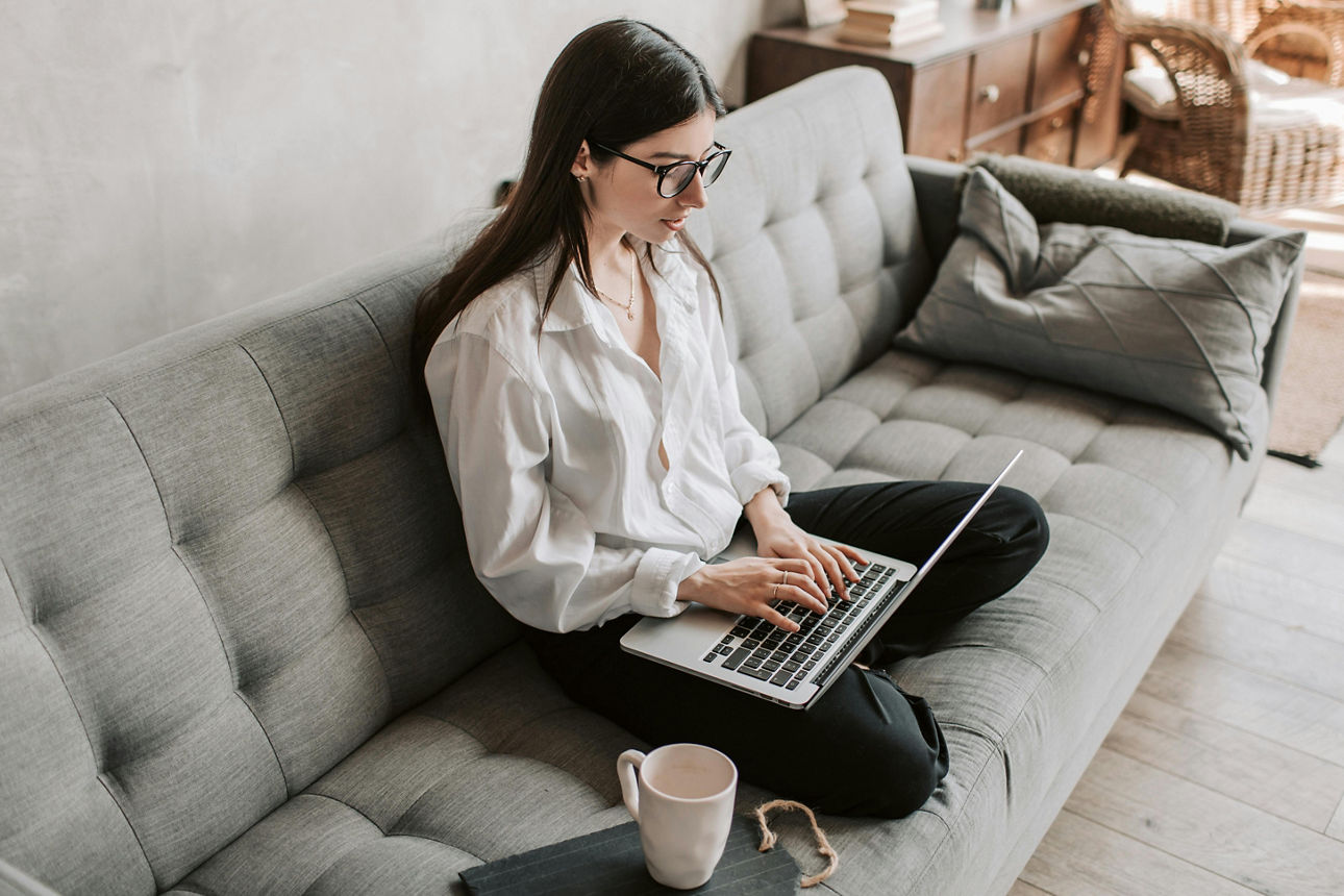 Eine junge Frau sitzt auf einem Sofa und arbeitet am Laptop
