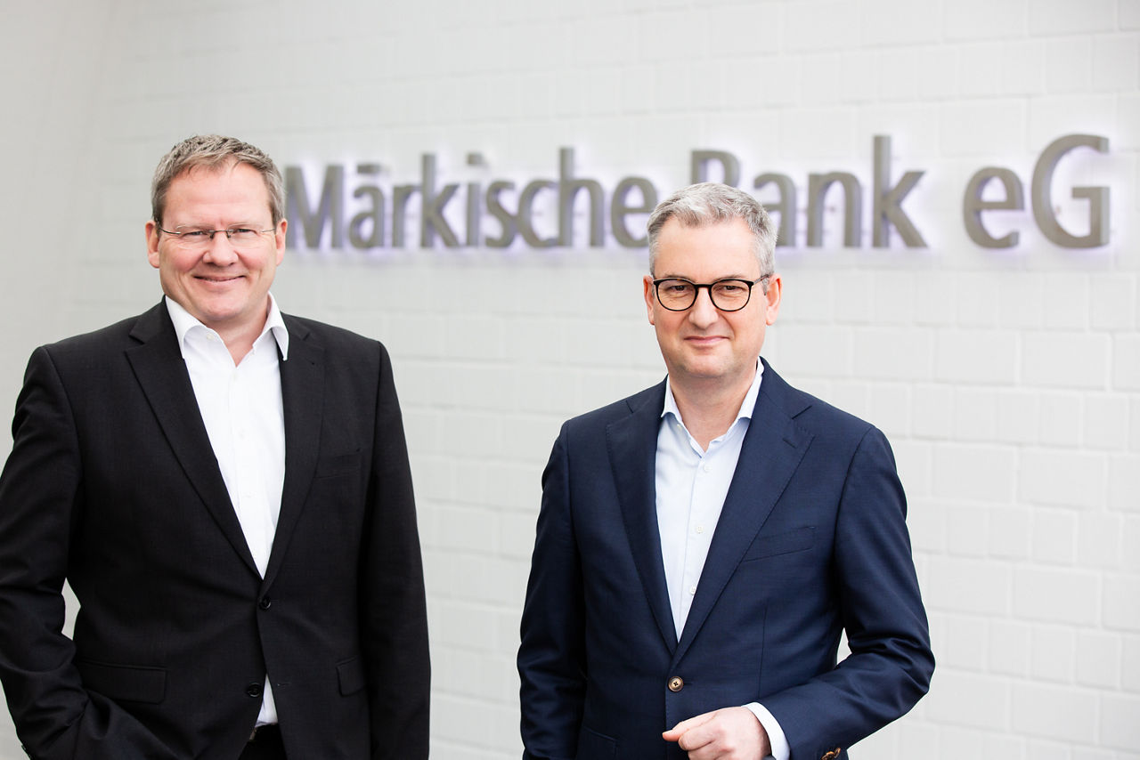 Achim Hahn und Arthur Merz stehen vor einer weißen Wand mit der Aufschrift Märkische Bank eG