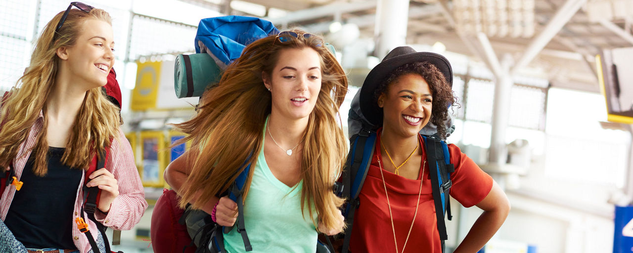 Drei junge Frauen mit Gepäck am Flughafen.
