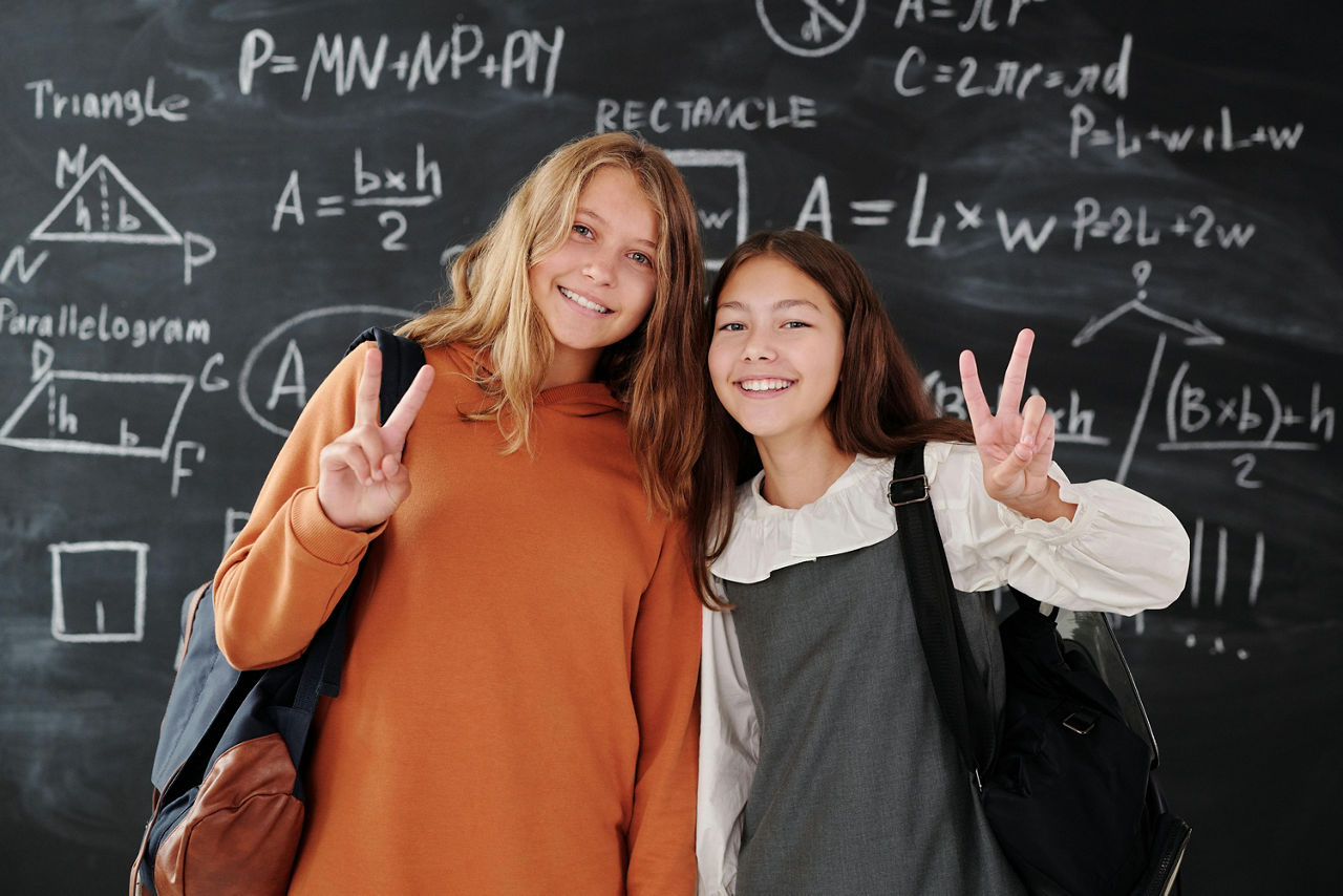 Zwei Mädchen, die vor einer Schultafel stehen und in die Kamera lächeln